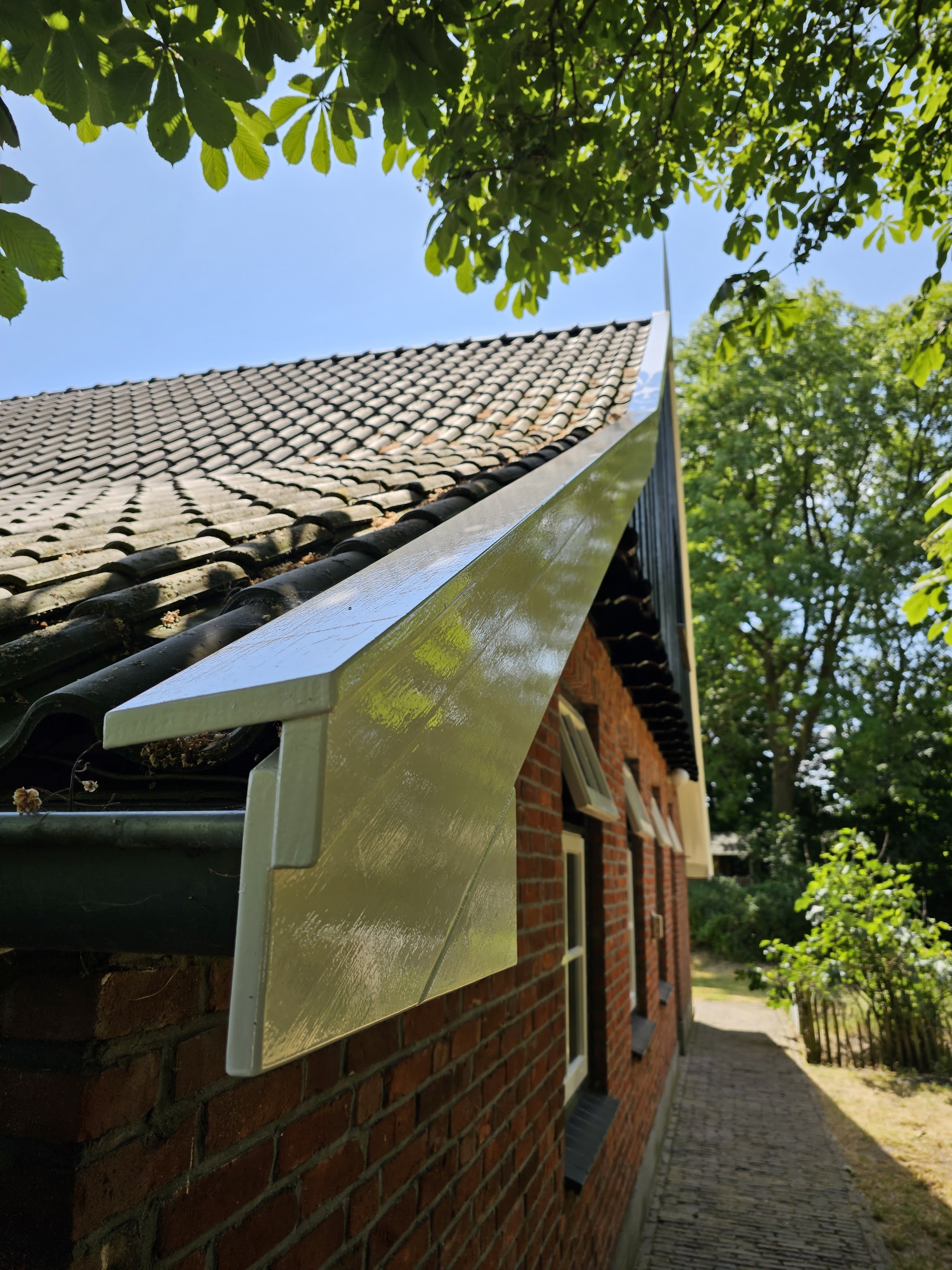 Wit afgewerkte zijwang van een dakkapel boven een bakstenen muur