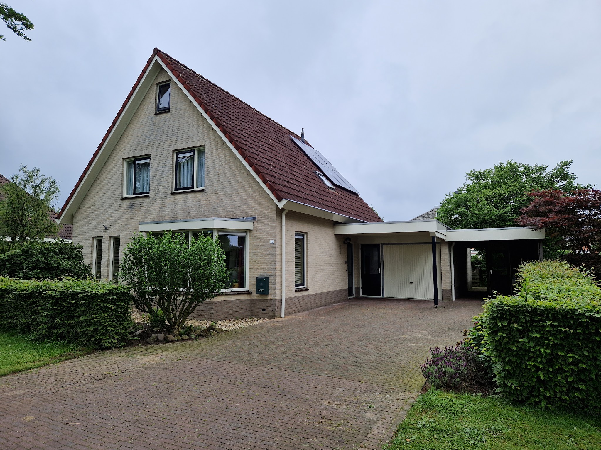 Geschilderde woning met puntdak, oprit en carport